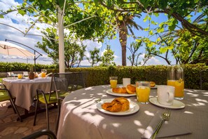 Un espace extérieur aménagé pour les repas, avec des tables, des chaises et une vue sur la mer.