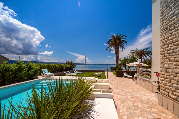 Un espace piscine avec vue sur la mer, des chaises longues et un mur en pierre.