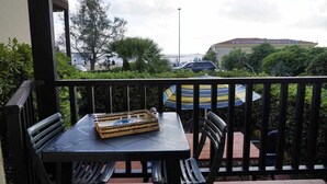 A balcony with a table and chairs, a striped umbrella, and a view of the sea and buildings. - Beachfront three room apartment with garden "Ostrica" (Alghero)