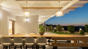 A modern dining area with a long wooden table, six white chairs, and two hanging light fixtures. -  Elaida Villa, Refined Group Escape • Pool & Play (Rethymno)