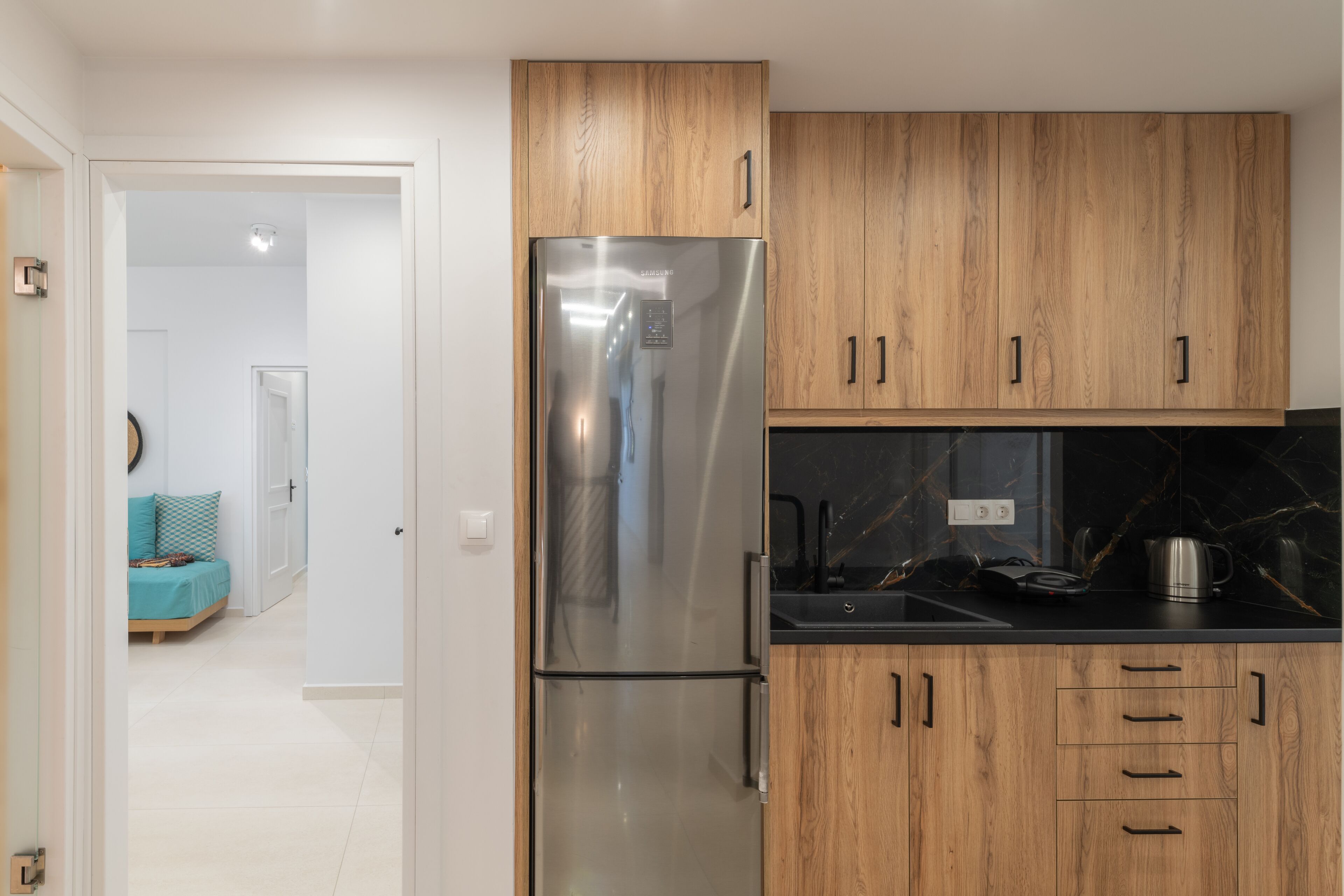 A modern kitchen with wooden cabinets, a stainless steel refrigerator, and a black countertop.