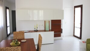 A modern kitchen with white cabinets, a dining table with chairs, and a small island with a candle holder. - IL VILLINO --- SWIMMING POOL NOT SHARED AND PRIVATE BEACH --- (Cefalù)