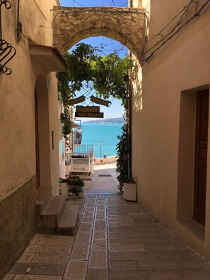Une ruelle étroite, surmontée d’une arche en pierre, qui mène à une plage.