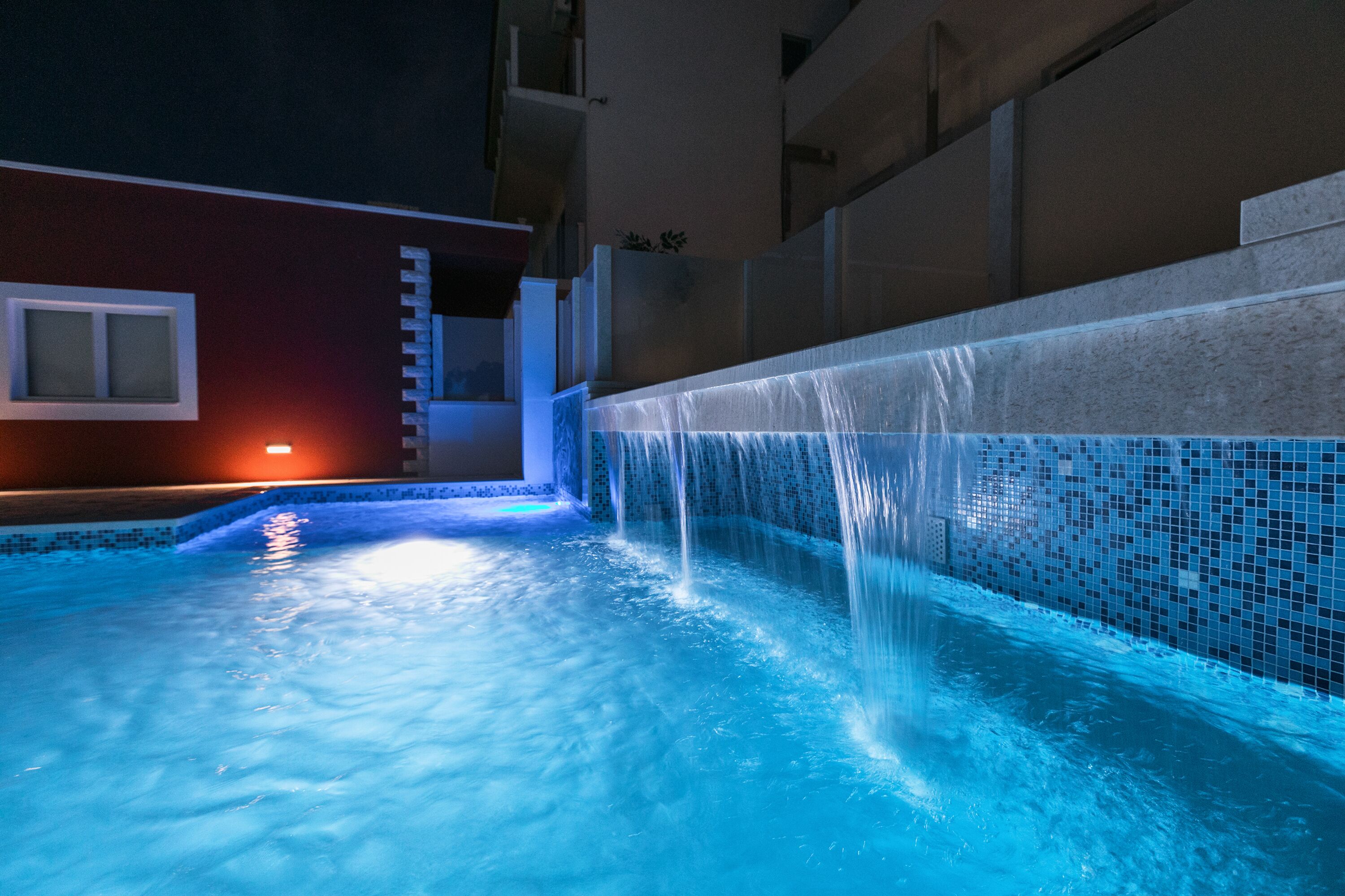 Ein Schwimmbecken mit Wasserspiel, einer Leiter und einer gefliesten Wand.