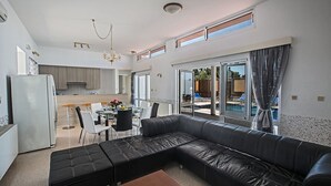 Ein modernes Wohnzimmer mit einem schwarzen Ledersofa, einem Essbereich mit Tisch und Stühlen sowie einer Küche im Hintergrund.