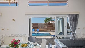 Ein Essbereich mit Tisch für vier Personen, einer Couch und Blick auf einen Swimmingpool und Sitzgelegenheiten im Freien.