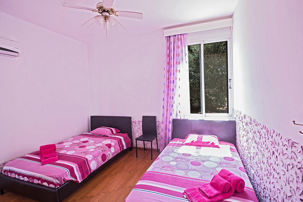 A bedroom with two single beds, a ceiling fan, a window with curtains, and a chair.