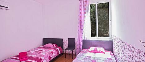 A bedroom with two single beds, a ceiling fan, a window with curtains, and a chair.