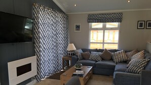 Una sala de estar con un sofá, una mesa de centro, un televisor y una ventana con cortinas.
