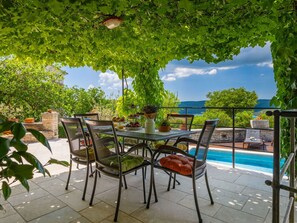 Un espace de restauration en plein air, avec une table et des chaises, entouré de verdure et donnant sur une piscine.