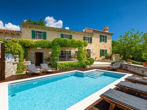 Vue sur un bâtiment avec piscine, espace de détente extérieur et verdure, prise depuis le bord de la piscine.