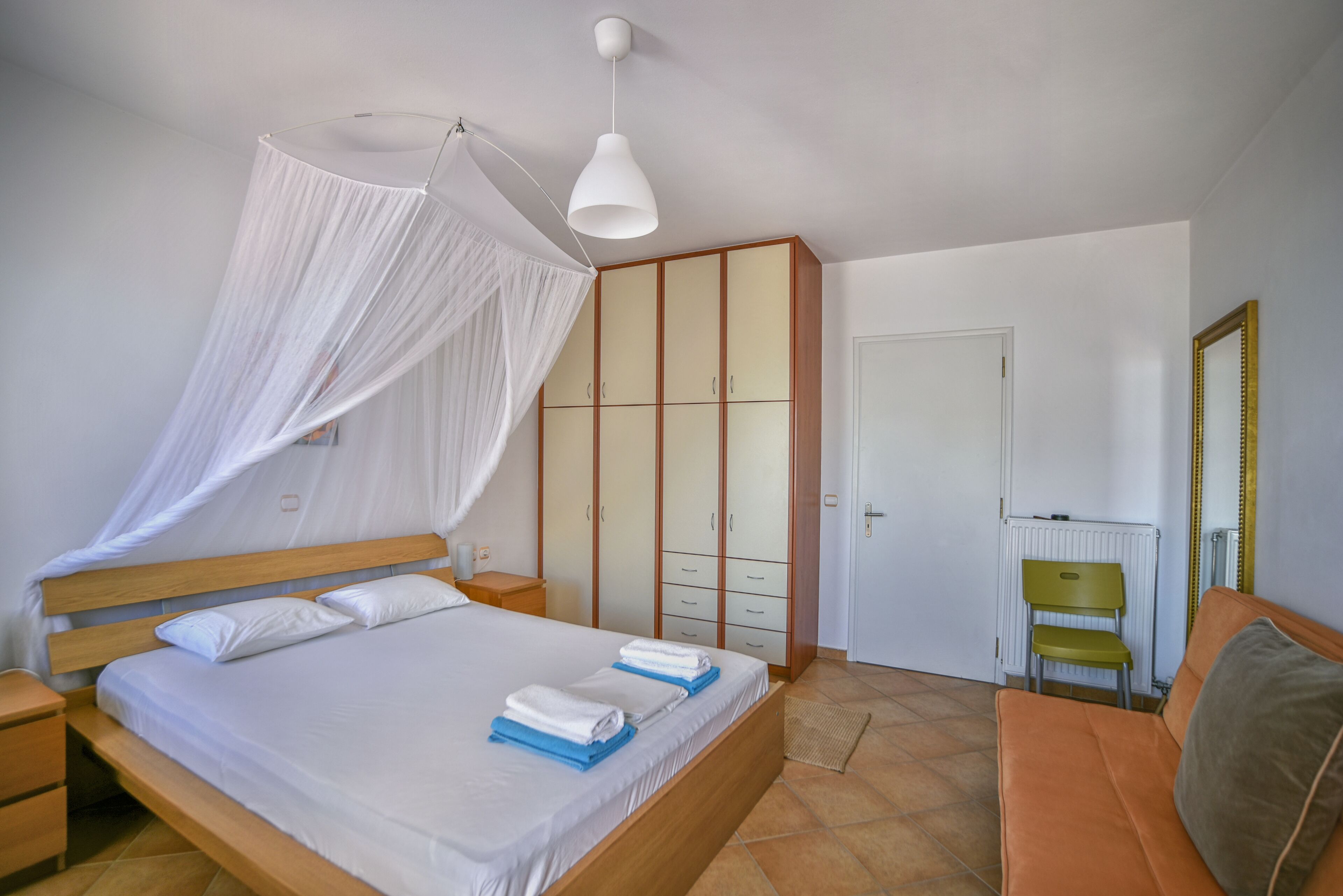 Una camera da letto con un letto, un comodino, una sedia, un armadio e uno specchio.