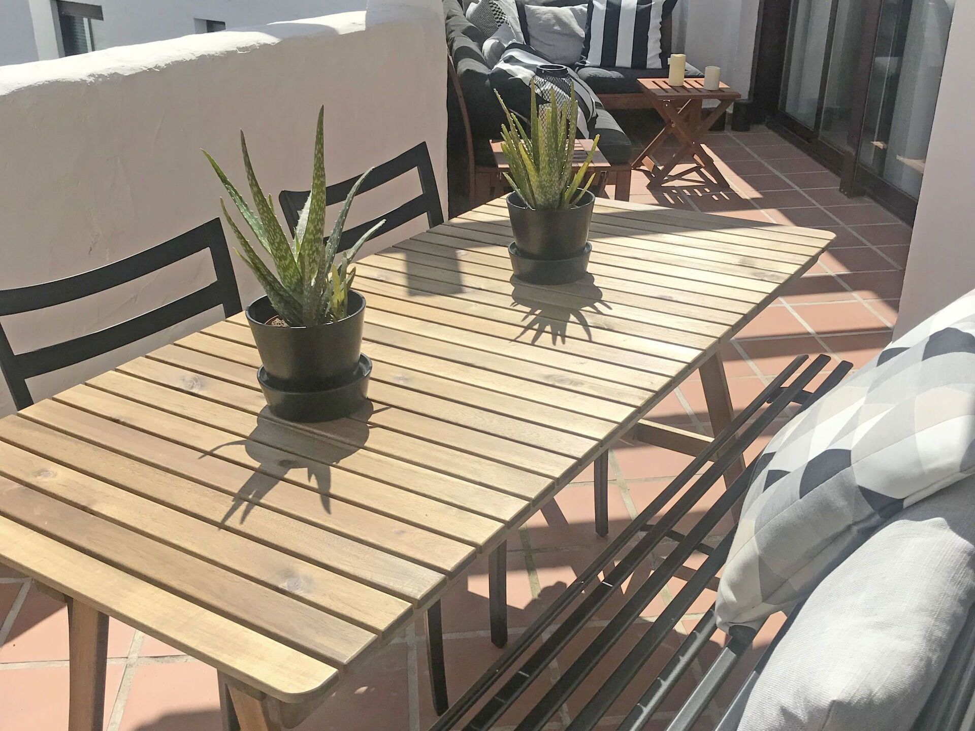 Una mesa de madera con dos plantas en macetas, una silla negra y un sofá con cojines a rayas.