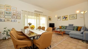 A living room with a dining area, a sofa, a TV, and framed pictures on the walls. - Cosy apartment for 5 people with WIFI, A/C, pool, TV, terrace and pets allowed (Solin)