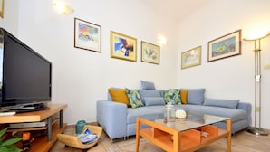 A living room with a flat-screen TV, a sofa with cushions, a glass coffee table, and artwork on the walls. - Cosy apartment for 5 people with WIFI, A/C, pool, TV, terrace and pets allowed (Solin)