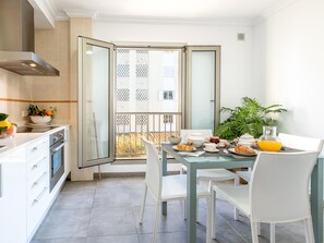 Une cuisine moderne équipée d’un four, une table à manger avec des chaises et un balcon offrant une vue sur les immeubles.