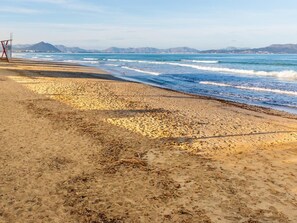 Une plage avec une tour de surveillance, des vagues et des montagnes à l’horizon.