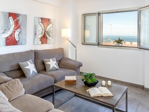 A modern living room with a sofa, coffee table, and artwork on the wall. - Apartamento Castello Playa · Your beachfront apartment in Can Picafort. (Can Picafort)