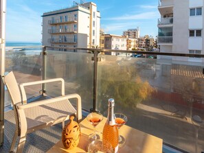 A balcony with a table set for two, a bottle, and glasses, overlooking a coastal cityscape. - Apartamento Castello Playa · Your beachfront apartment in Can Picafort. (Can Picafort)