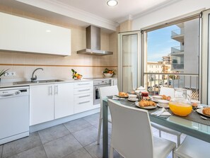A modern kitchen with a dishwasher, stove, and a dining area with breakfast items. - Apartamento Castello Playa · Your beachfront apartment in Can Picafort. (Can Picafort)