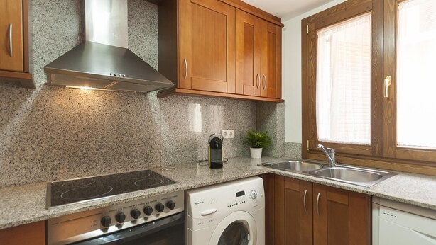 A kitchen with granite countertops, wooden cabinets, a stainless steel range hood, a built-in oven, a washing machine, and a sink. - NEW APARTMENT CLOSE TO THE BEACH 2 (Tossa de Mar)
