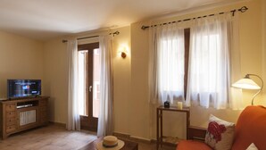A living room with a television on a wooden cabinet, a wooden coffee table, an orange sofa with decorative pillows, and a small table with a candle and a book. - NEW APARTMENT CLOSE TO THE BEACH 2 (Tossa de Mar)