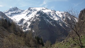 Een bergachtig landschap met besneeuwde toppen, rotsachtig terrein en schaarse begroeiing.