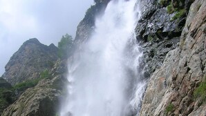 Een gezin poseert voor een waterval met rotsachtig terrein en groen in de achtergrond.