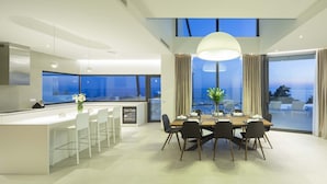 A modern dining area with a large table set for six, a kitchen counter, and a view of the sea through large windows. - 5*Familiy Villa,Seaview,Indoor&Outdoor Heated Pools (Makarska)