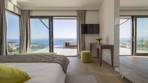 A modern hotel room with a large bed, a sofa, a desk, and a TV. The room has large windows offering a view of the city and the sea. - 5*Familiy Villa,Seaview,Indoor&Outdoor Heated Pools (Makarska)