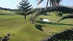 Golfkenttä, jossa on hiekkabunkkeri, mänty ja kirkas taivas.