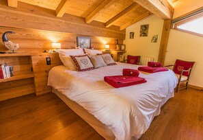 A cozy bedroom with a wooden ceiling, a large bed with white linens, red towels, and heart-shaped pillows.