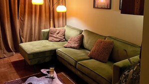 A room with a green sofa, two pendant lights, a framed picture, and a wooden sideboard. - Charming and modern vintage style apartment located in prime location! (Antwerpen)