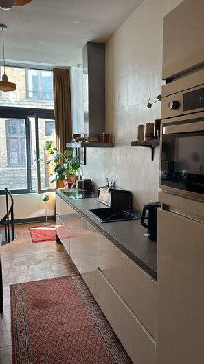 A modern kitchen with a large window, a built-in oven, and a countertop with various appliances. - Charming and modern vintage style apartment located in prime location! (Antwerpen)