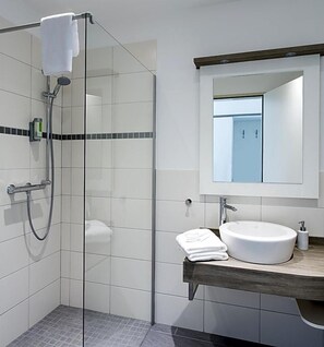 A modern bathroom with a glass shower enclosure, a white sink, and a wooden countertop.