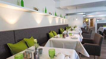 Ein Restaurant mit mehreren Tischen, ausgestattet mit grünem Glas, weißen Tischdecken und grau gepolsterten Stühlen.
