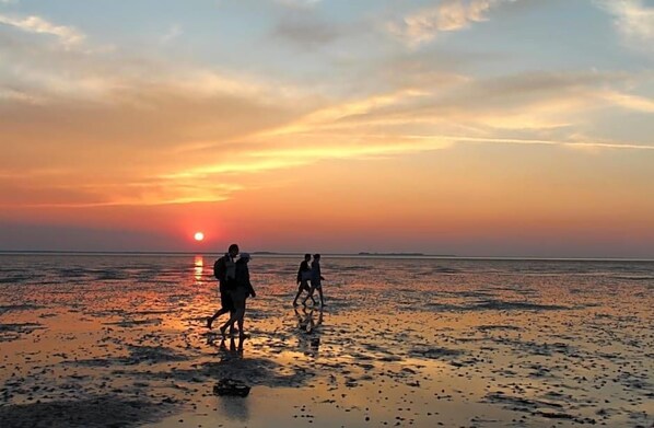 A beach scene with people walking during sunset.