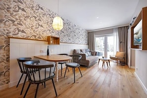 Un espace de vie moderne comprenant un coin repas, un canapé et une grande fenêtre laissant entrer la lumière naturelle.
