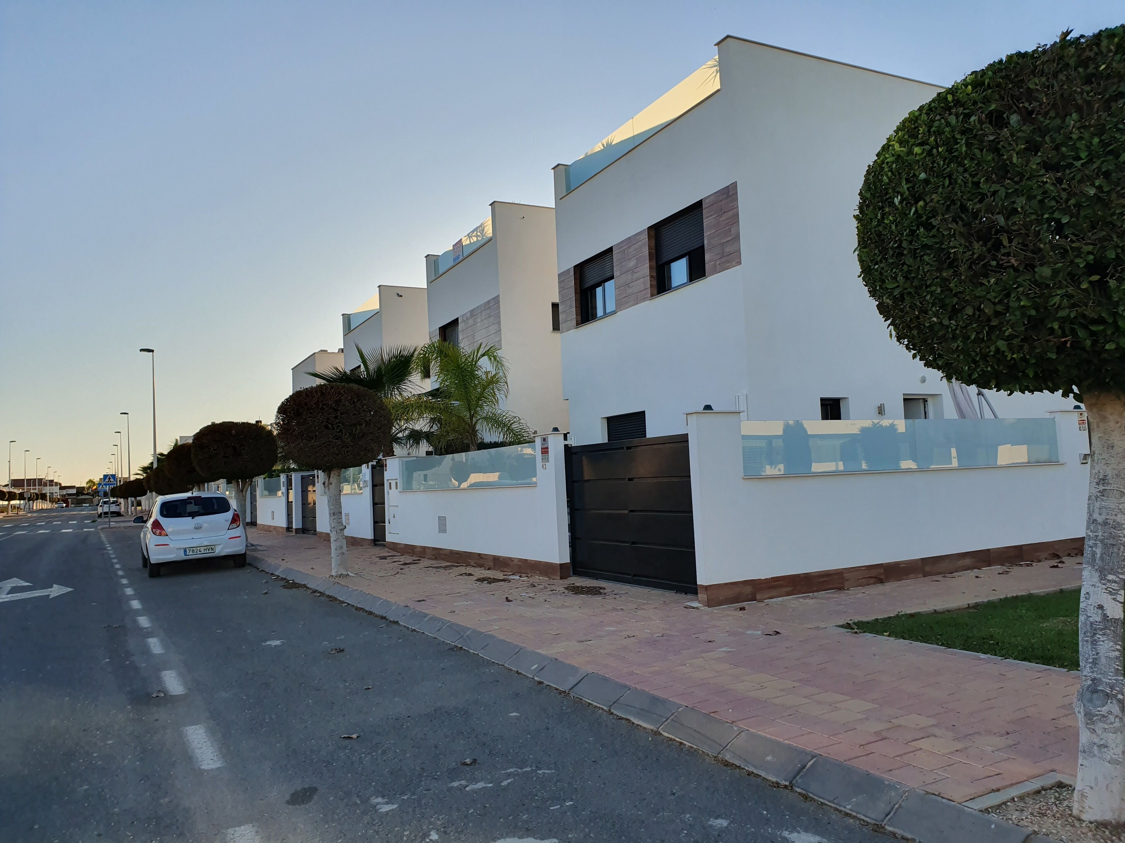 A modern building with a white facade, a black gate, and a car parked on the street.