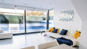 A modern living room with a white sofa, clear glass coffee table, and a view of an outdoor swimming pool through large sliding glass doors. - Luxury Villa Pool, 10 mins Walk to Beach & Golf near by (San Pedro del Pinatar)