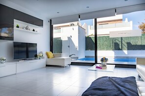A modern living room with a flat-screen TV, white sofas, a coffee table, and a view of a swimming pool. - Luxury Villa Pool, 10 mins Walk to Beach & Golf near by (San Pedro del Pinatar)