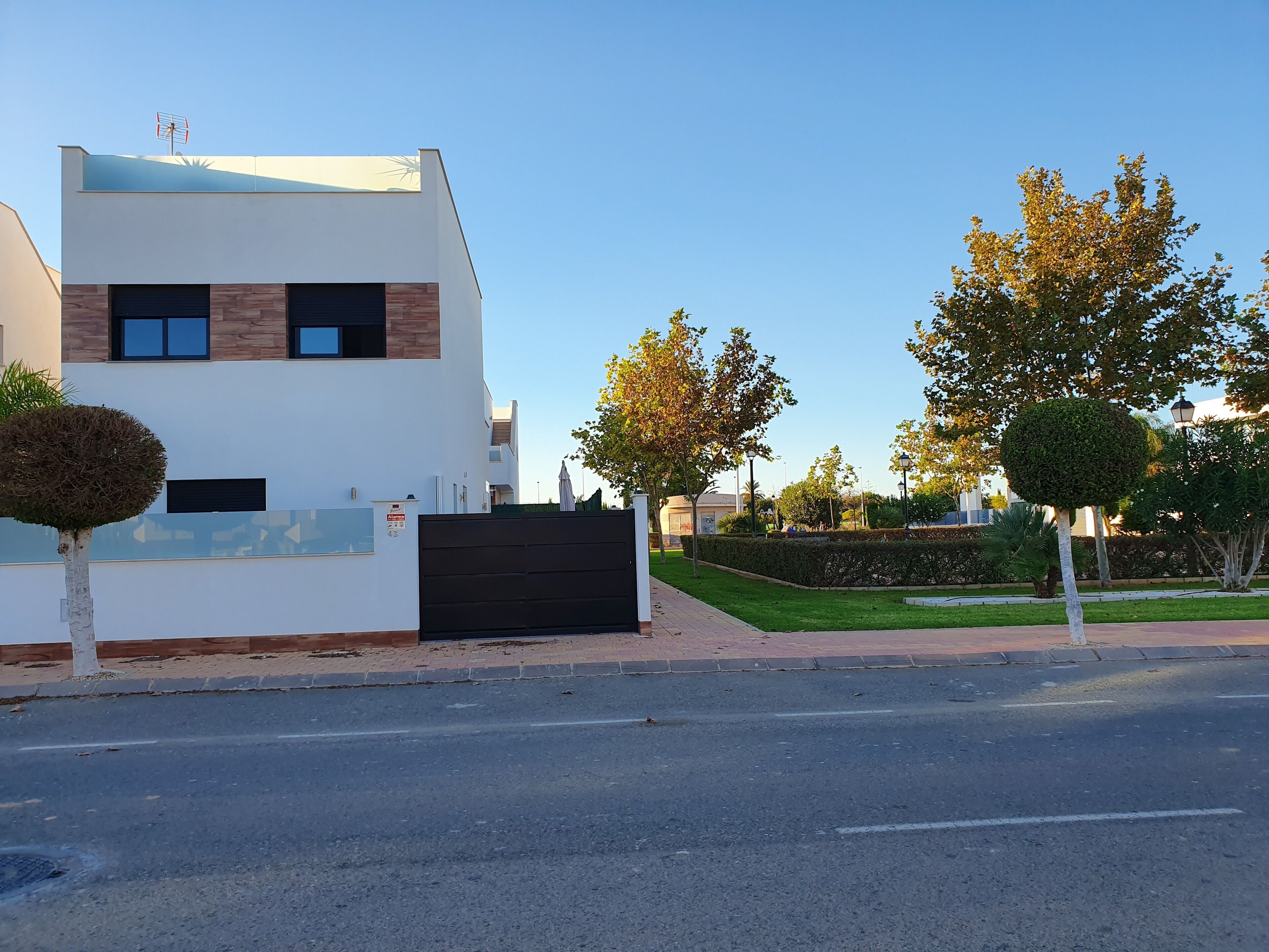 Un edificio moderno de dos pisos con techo plano, ventanas grandes y un portón negro.
