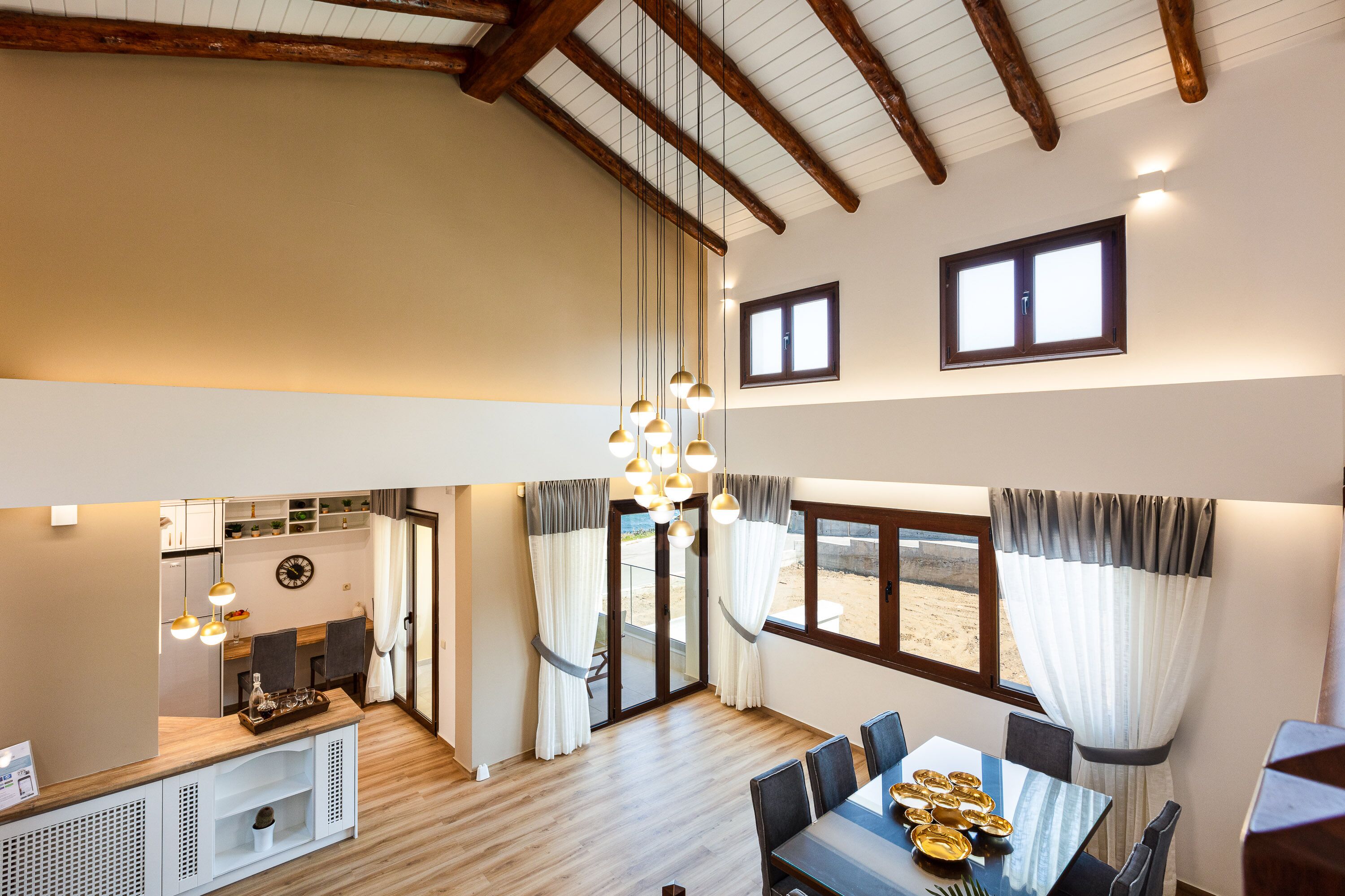 A spacious dining area with a high ceiling and wooden beams, a kitchen with modern appliances, and large windows offering a view of the beach.