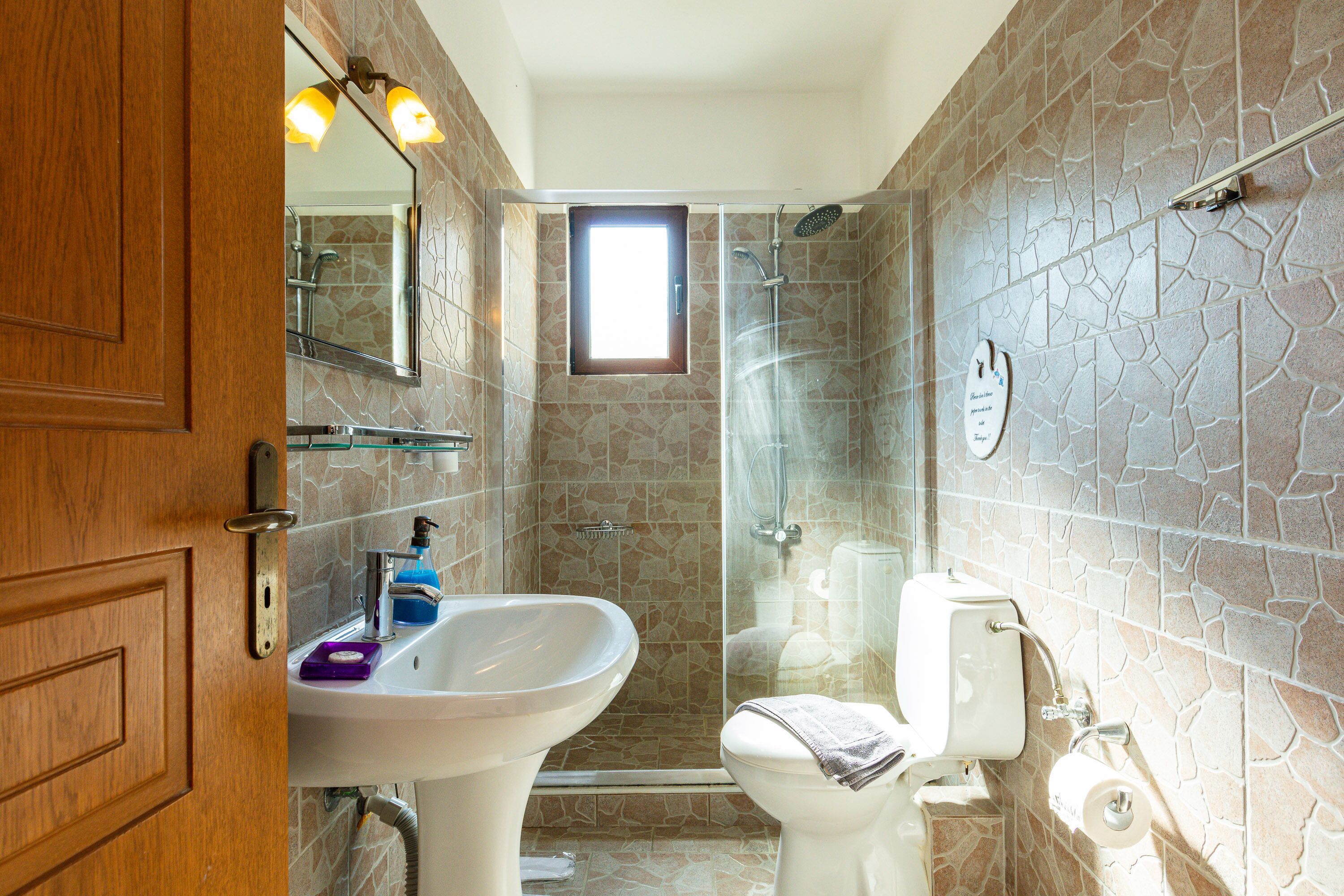 Une salle de bain avec une douche carrelée en pierre, un lavabo blanc et des toilettes.