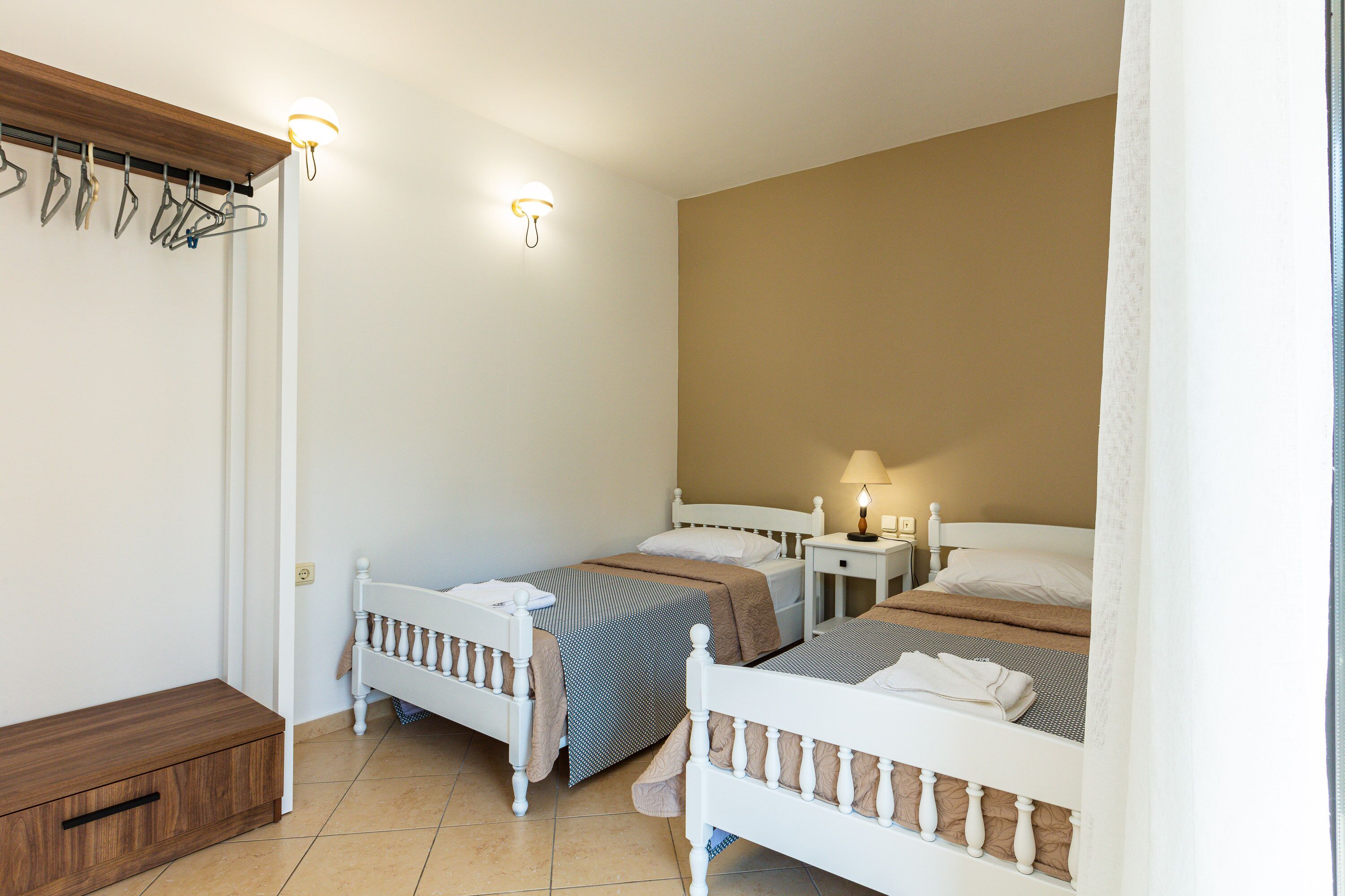 A bedroom with two single beds, a wooden bench, a wall-mounted drying rack, and a bedside table with a lamp.