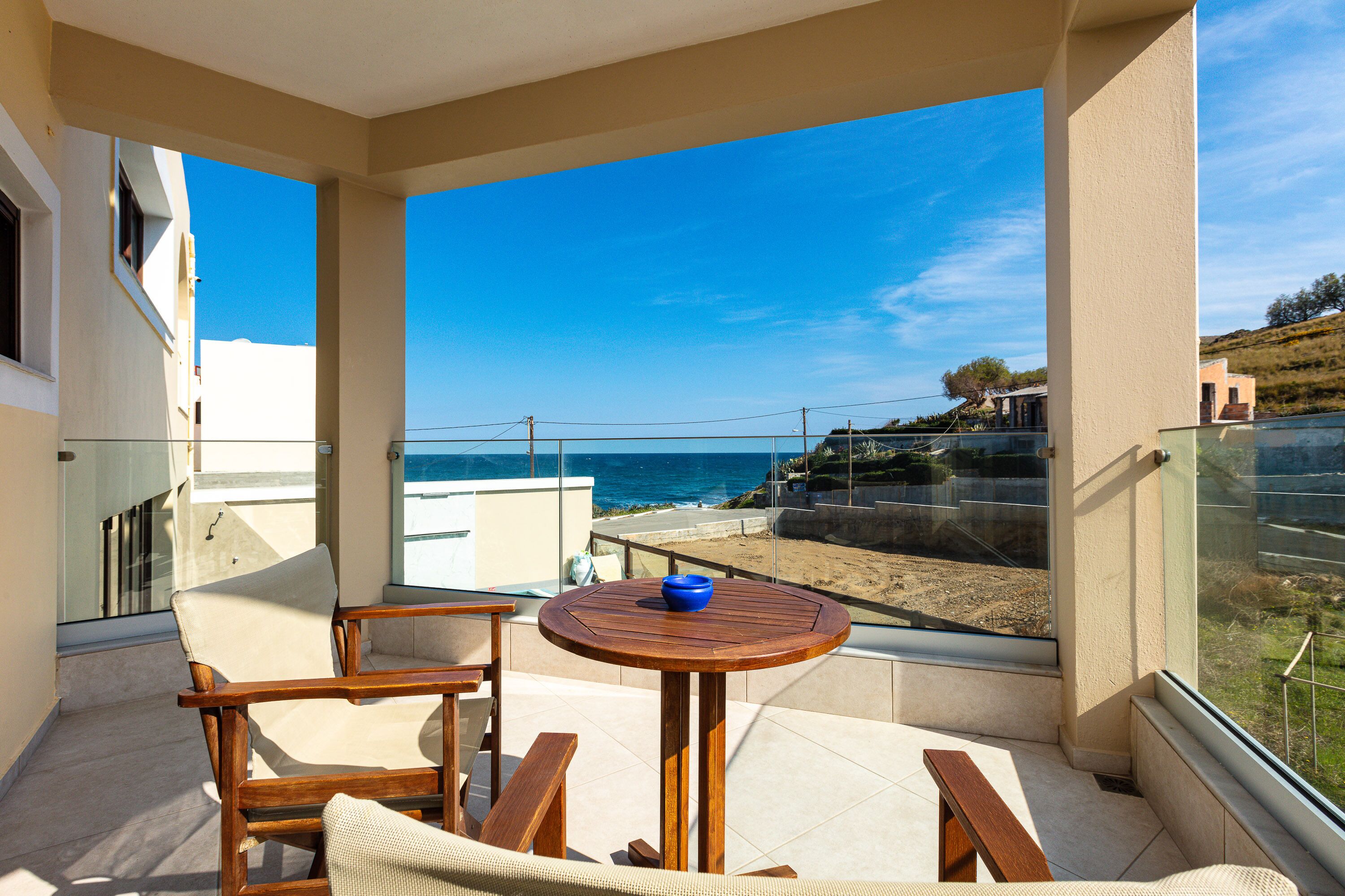 A balcony with a wooden table and chairs, a blue bowl, and a view of the beach and ocean.