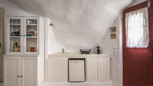 A compact kitchen with white cabinetry, a small sink, and a refrigerator. There is a wooden door with a decorative window treatment. - Traditional Farmers Secret Cave #1 (SANTORINI)