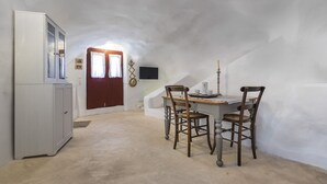 A narrow attic room with a dining table and chairs, a white cabinet, and a red door with lace curtains. - Traditional Farmers Secret Cave #1 (SANTORINI)