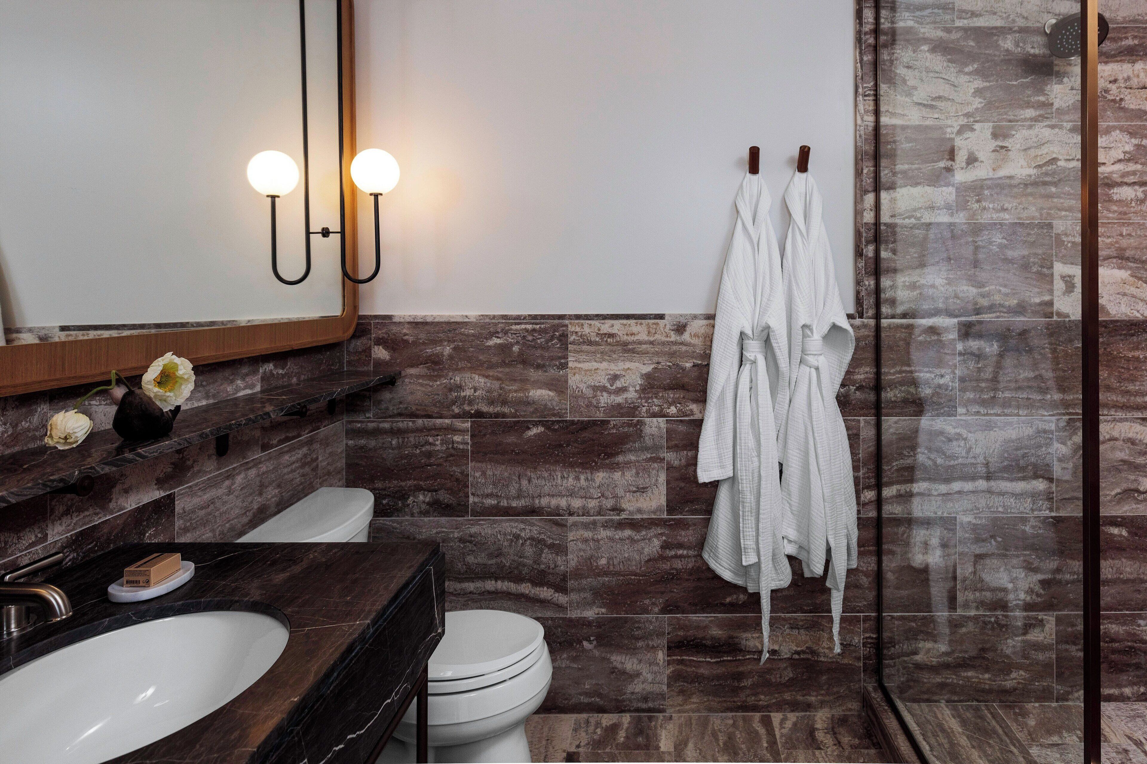 A modern bathroom with a large mirror, two wall-mounted lights, a white sink, a toilet, and a shower area with a glass door.