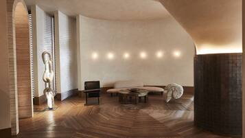 A modern interior with a herringbone wood floor, a sculptural piece, a sofa, a chair, and a round table.